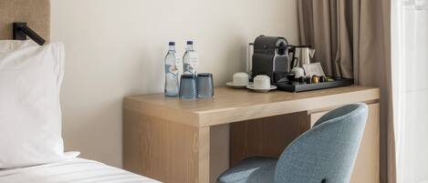 A hotel room with a bed, a desk with a coffee maker, two bottles, and a chair.