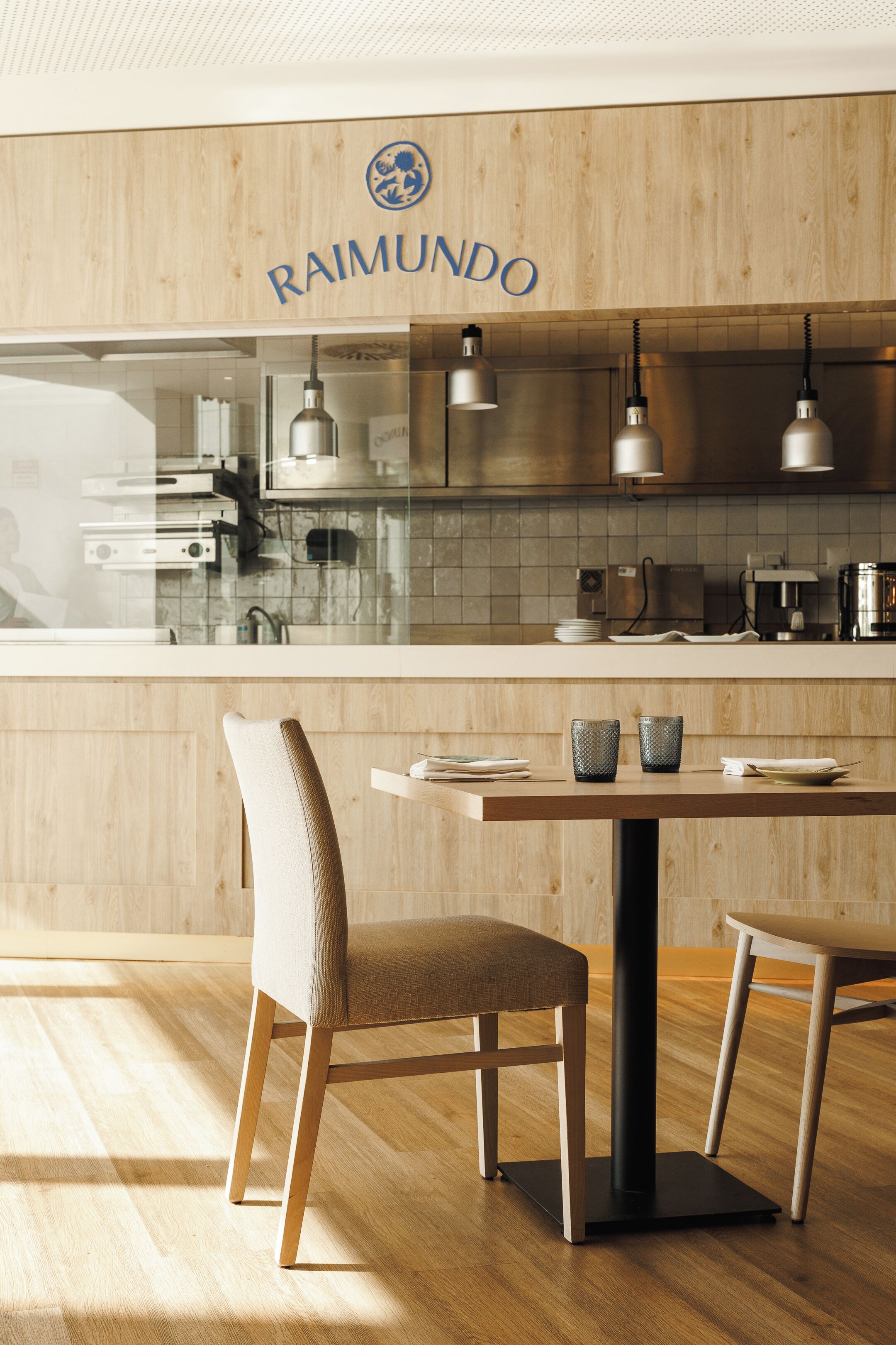A modern kitchen with wooden cabinetry, a countertop, and a dining area with two chairs and a table.