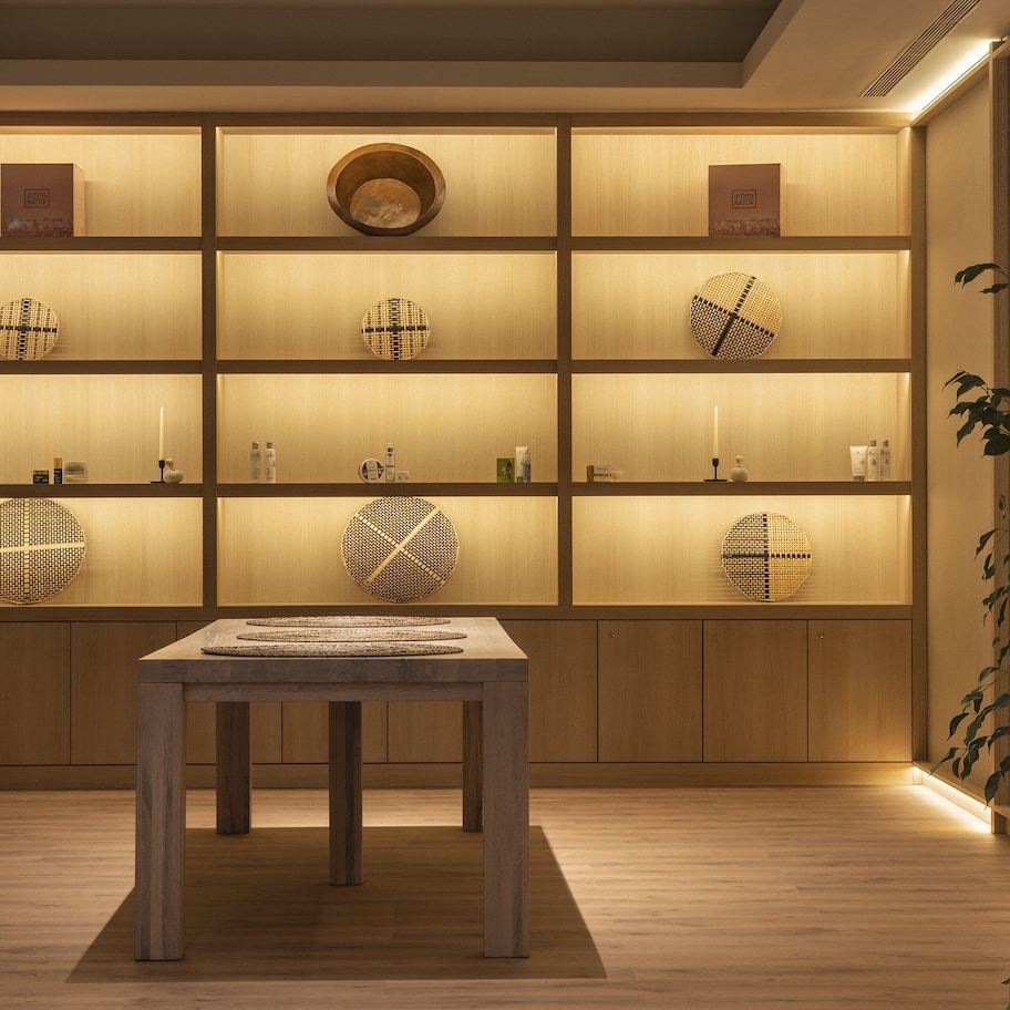 A room with a wooden floor, a central table, and a wall with shelves displaying various items.