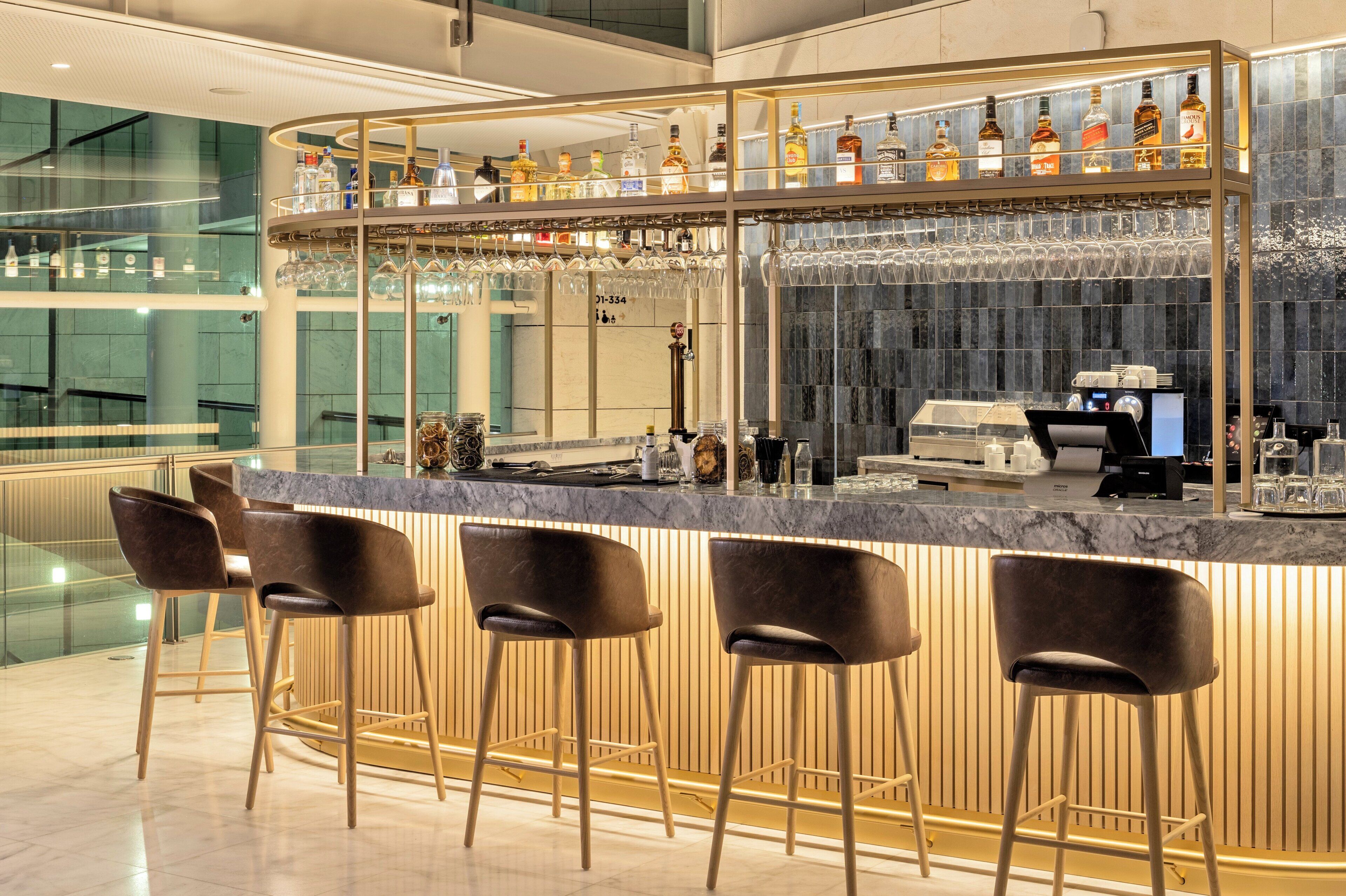 A bar area with a marble countertop, bar stools, and a variety of liquor bottles.