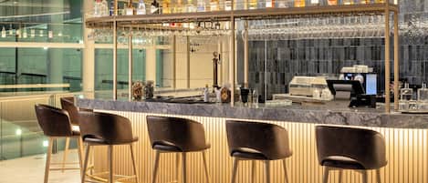A bar area with a marble countertop, bar stools, and a variety of liquor bottles.