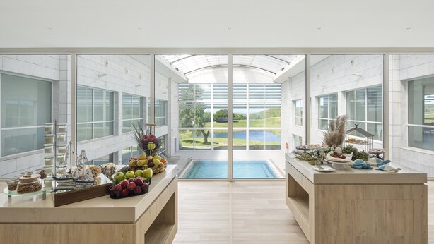 A modern kitchen with a central island, large windows, and a view of a pool and landscape. - Crowne Plaza Caparica Lisbon by IHG (Almada)
