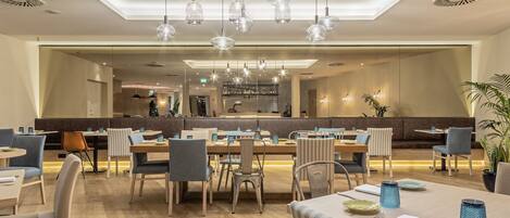 A modern restaurant with a central bar area, high ceilings, and contemporary lighting fixtures.