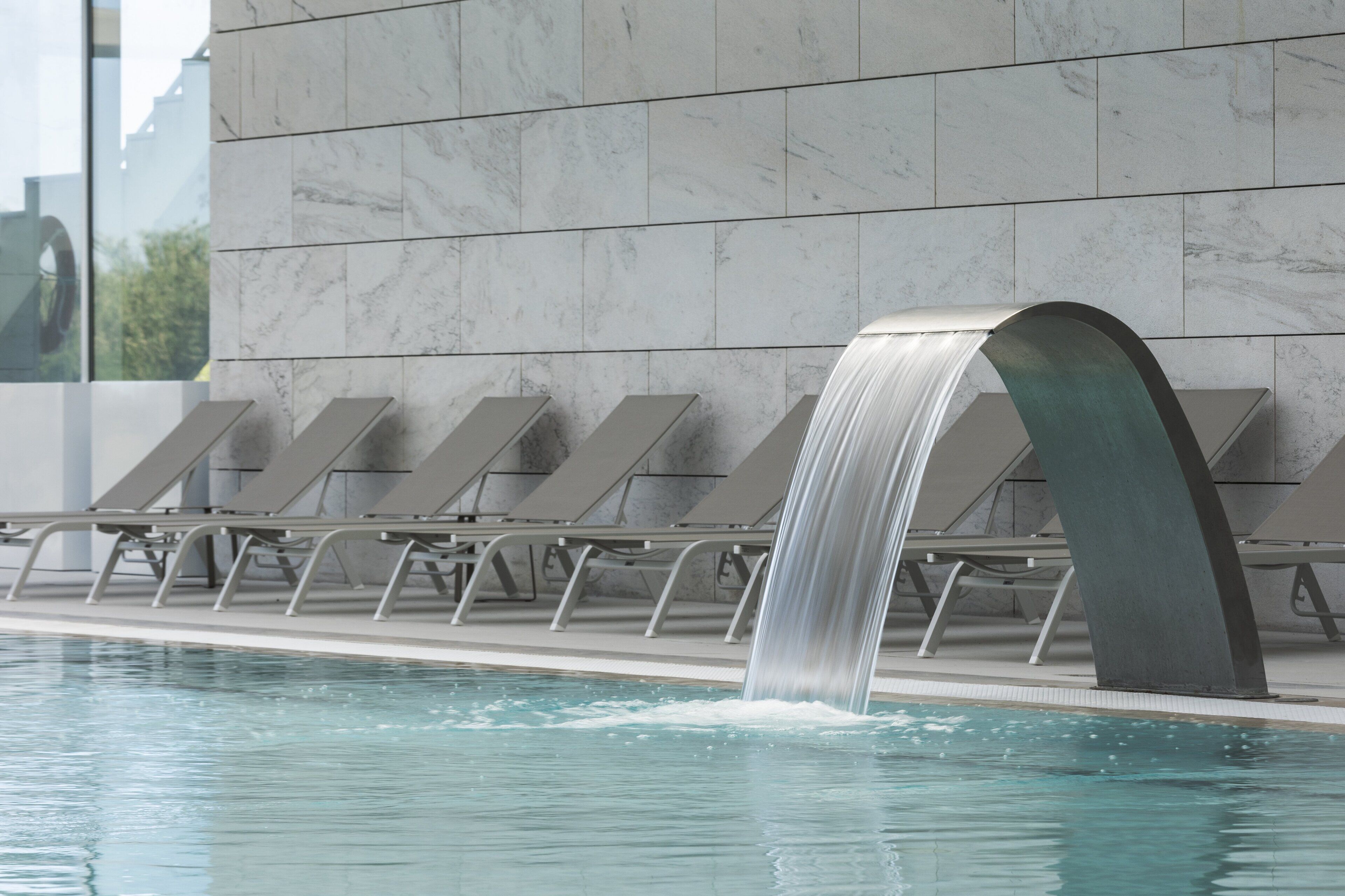 A pool with a waterfall feature, lounge chairs, and a marble wall.