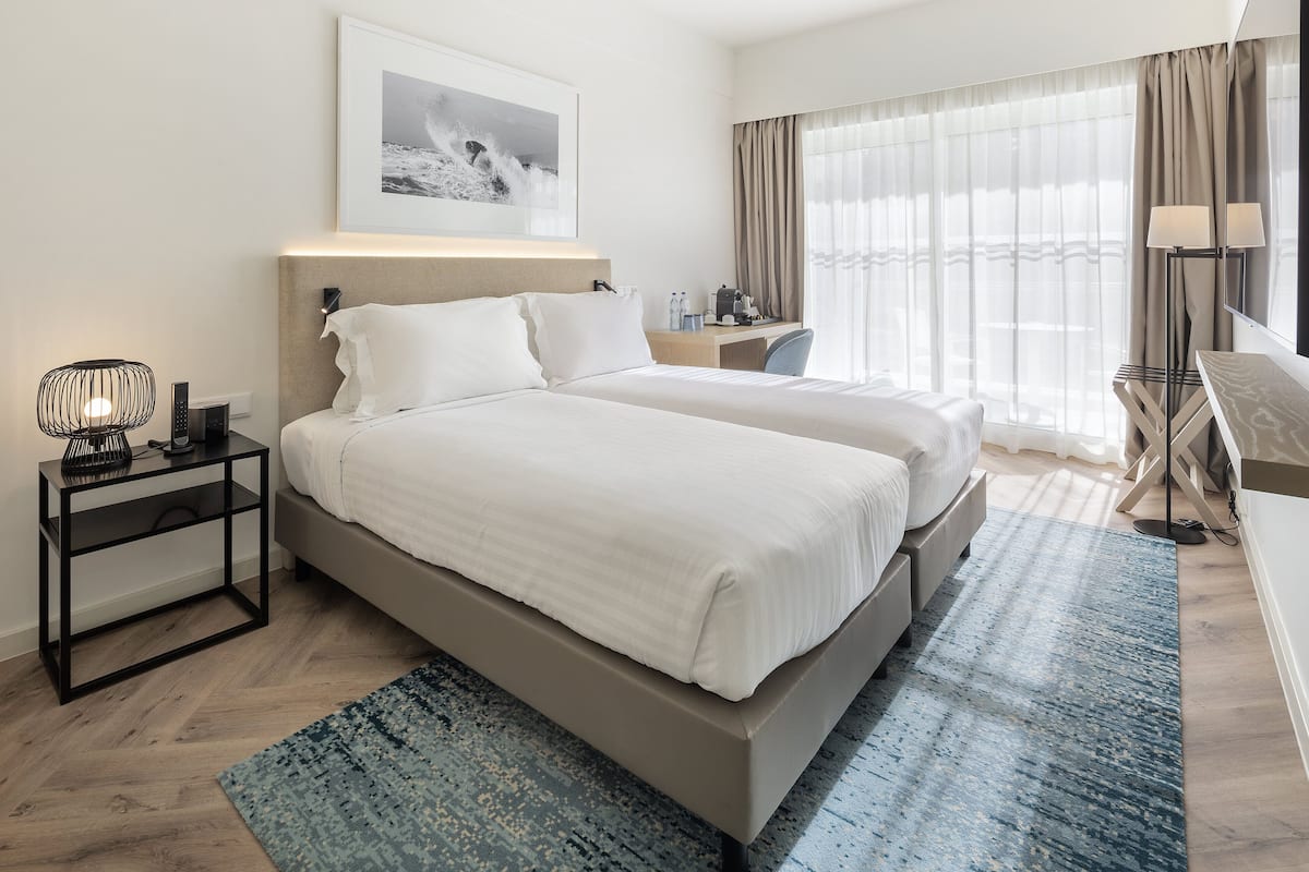 A modern hotel room with a large bed, bedside tables, a desk, and a window with curtains.