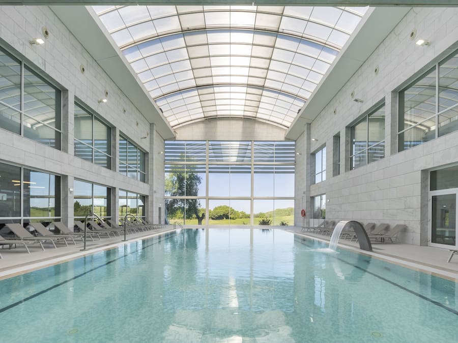 Una piscina interior con techo de cristal, vistas despejadas del exterior y tumbonas a lo largo de los bordes.