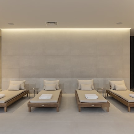 A modern hotel room with four single beds arranged in a row, each with a wooden frame and a white mattress.