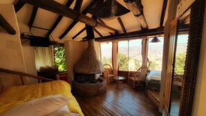 A cozy room with a bed, a fireplace, wicker chairs, and a view of the landscape. - Casa de Campo Cusco (Cusco)