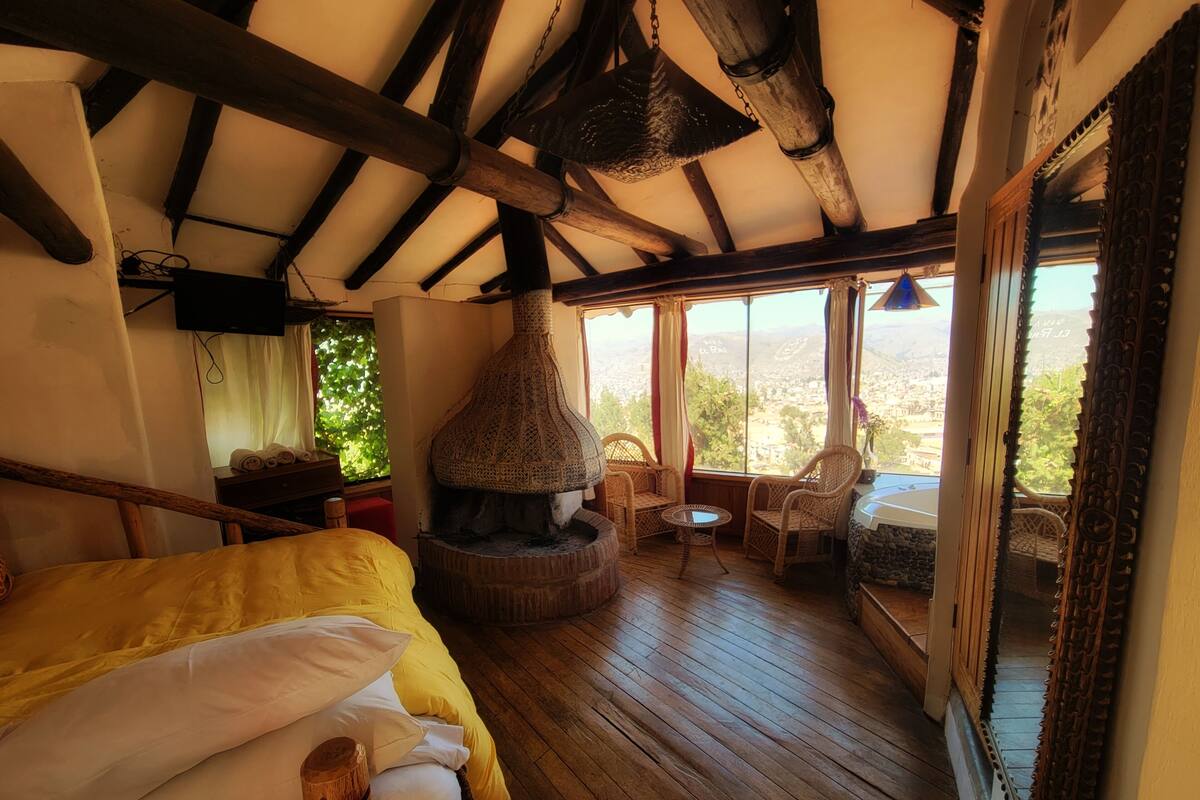 Ein gemütliches Zimmer mit einem Bett, einem Kamin, Korbstühlen und Blick auf die Landschaft.