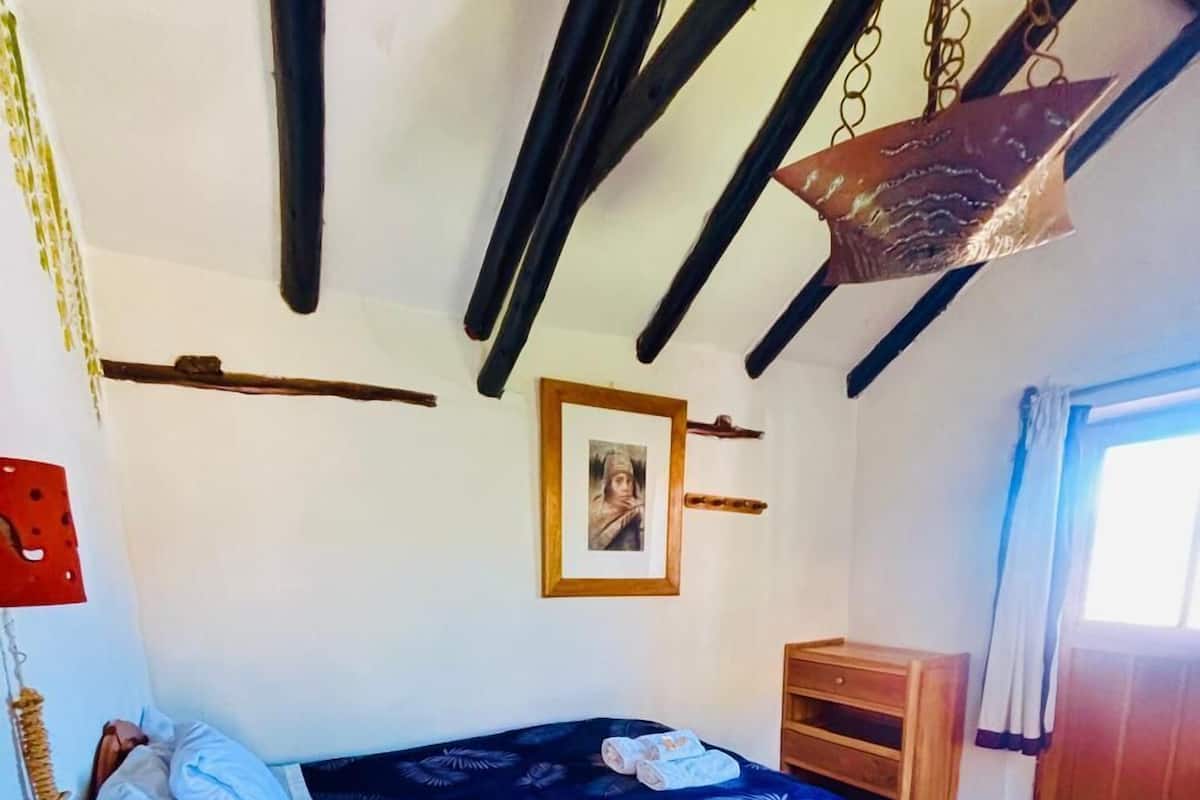 Ein Schlafzimmer mit Bett, Holz-Kopfteil, einer Pendelleuchte, einem gerahmten Bild an der Wand und einem Holzschrank.