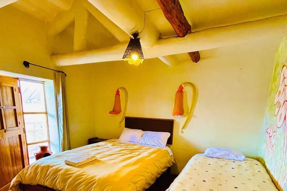 Ein Zimmer mit zwei Betten, Holzboden und einer schrägen Decke mit sichtbaren Balken.
