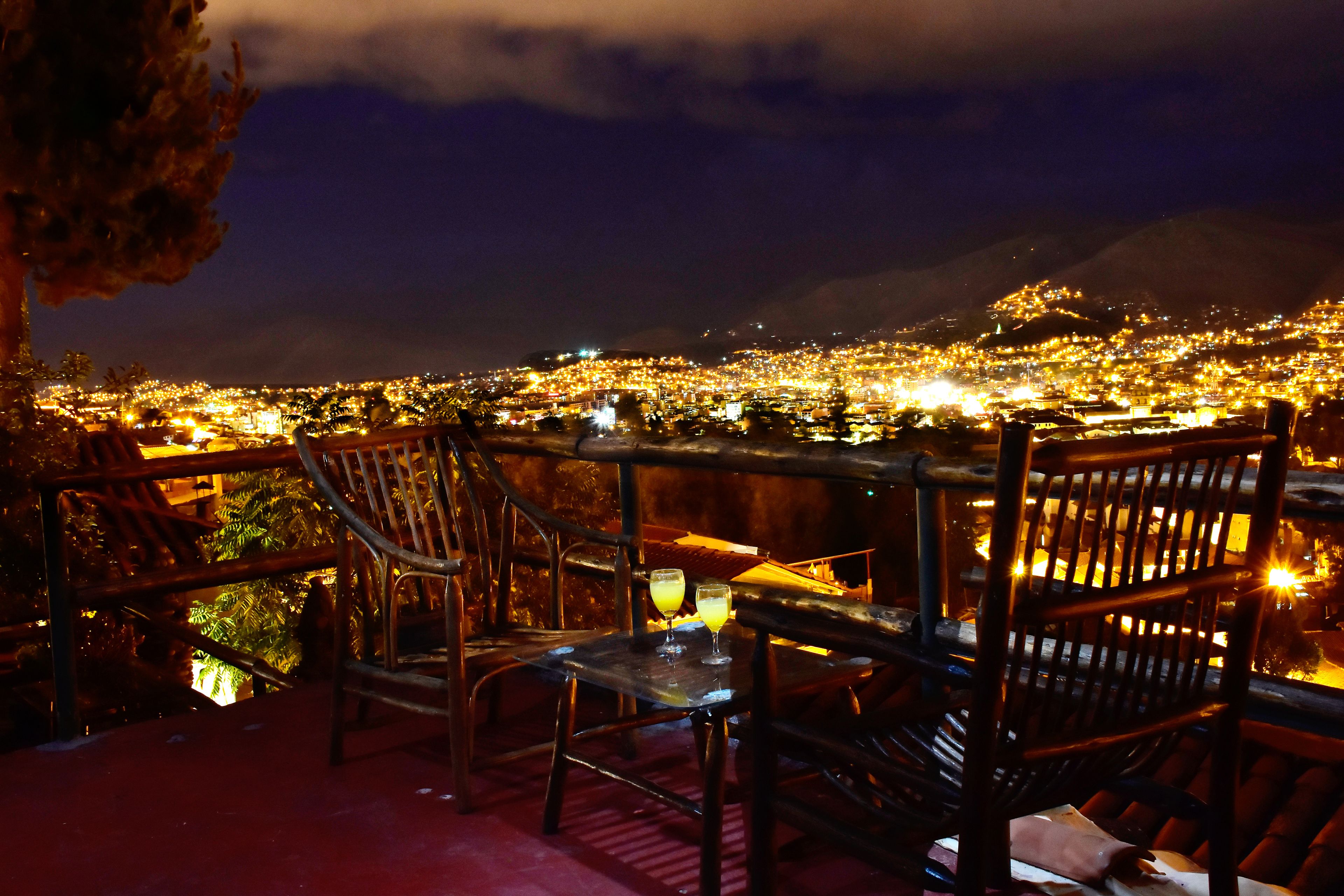Una terrazza con sedie e tavolo di legno, affacciata su un panorama urbano notturno.