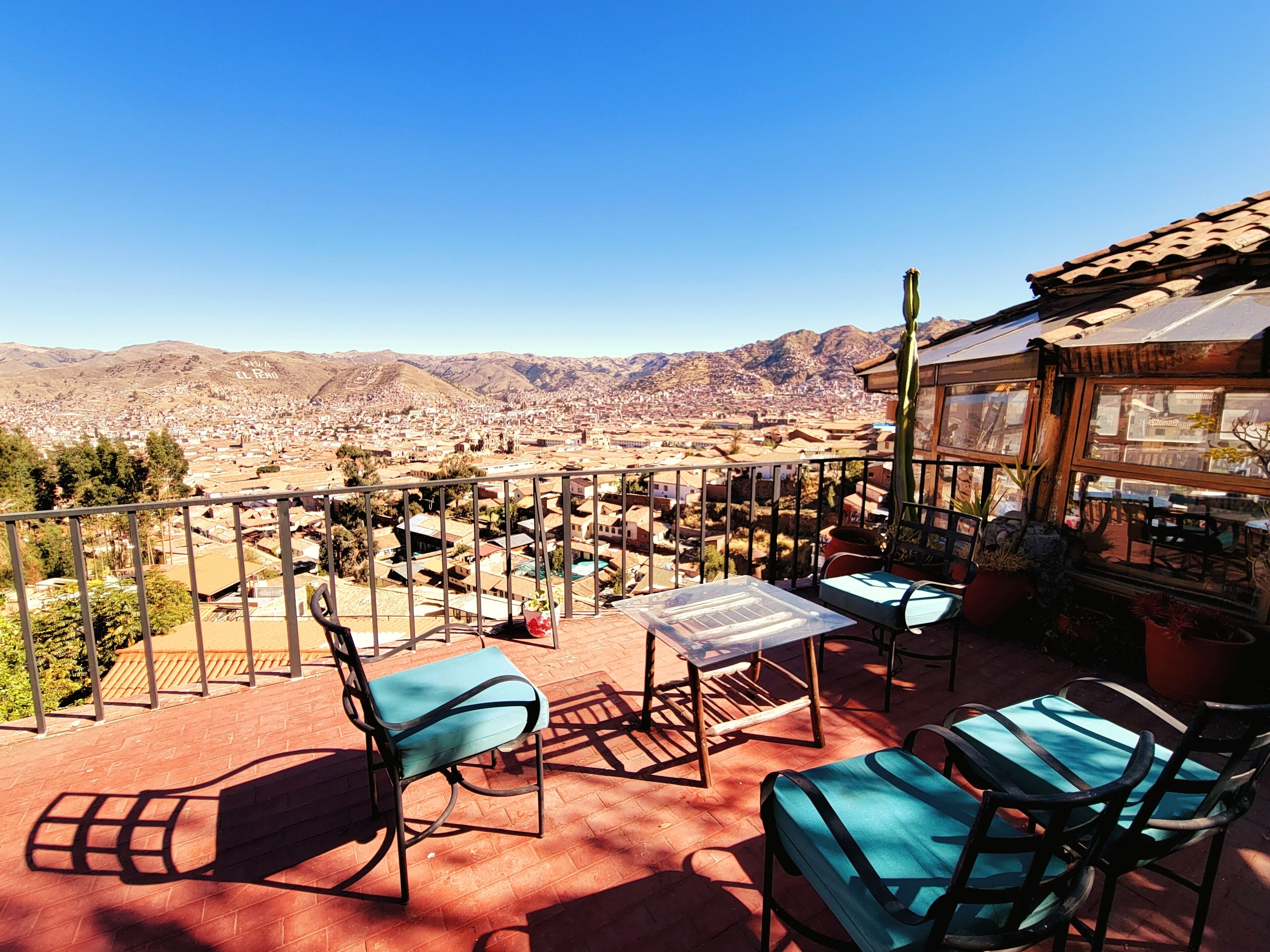 A balcony with a view of a city and mountains. There are two chairs and a table.