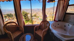 A room with a large window offering a view of a cityscape and mountains. There are wicker chairs and a bathtub. - Casa de Campo Cusco (Cusco)