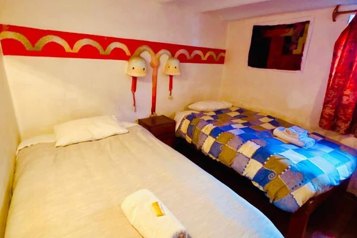 Ein Hotelzimmer mit zwei Betten, einem rot-weißen Kopfteil, zwei Wandlampen und einem kleinen Fenster.