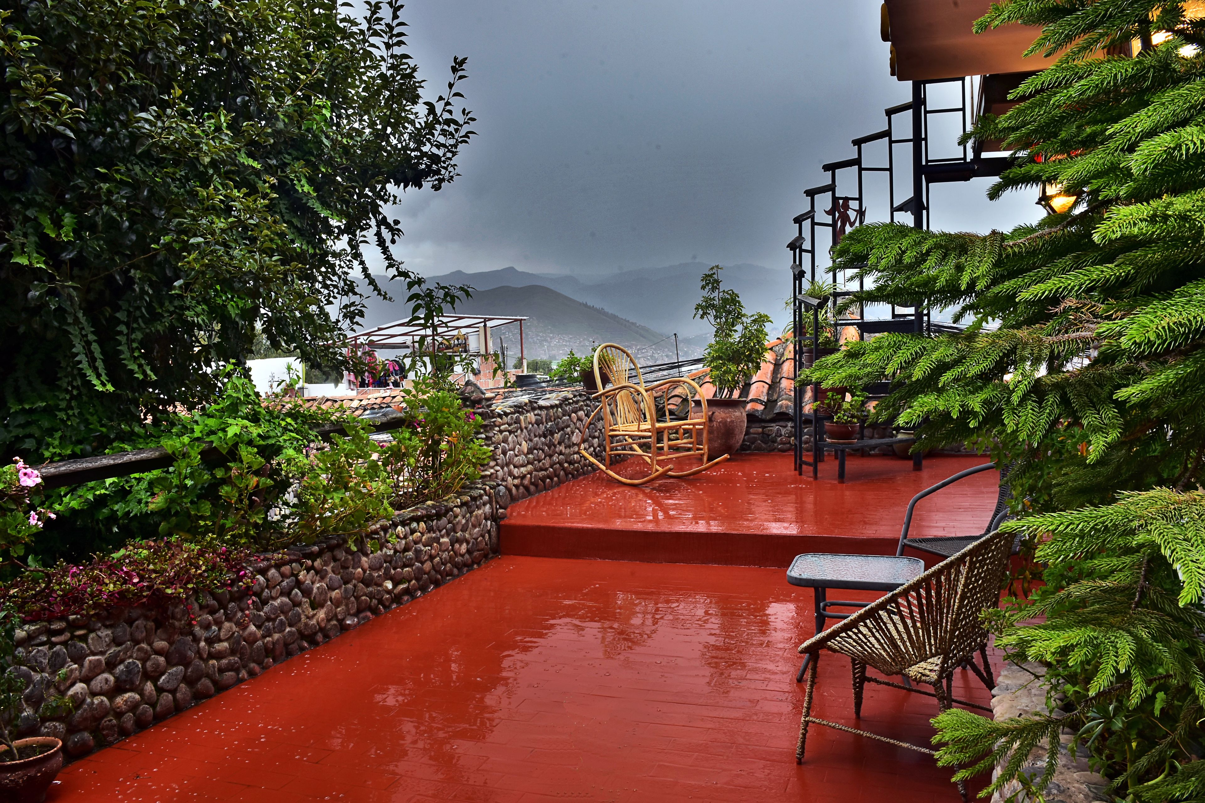 A red-tiled patio with outdoor seating, surrounded by greenery and a stone wall.