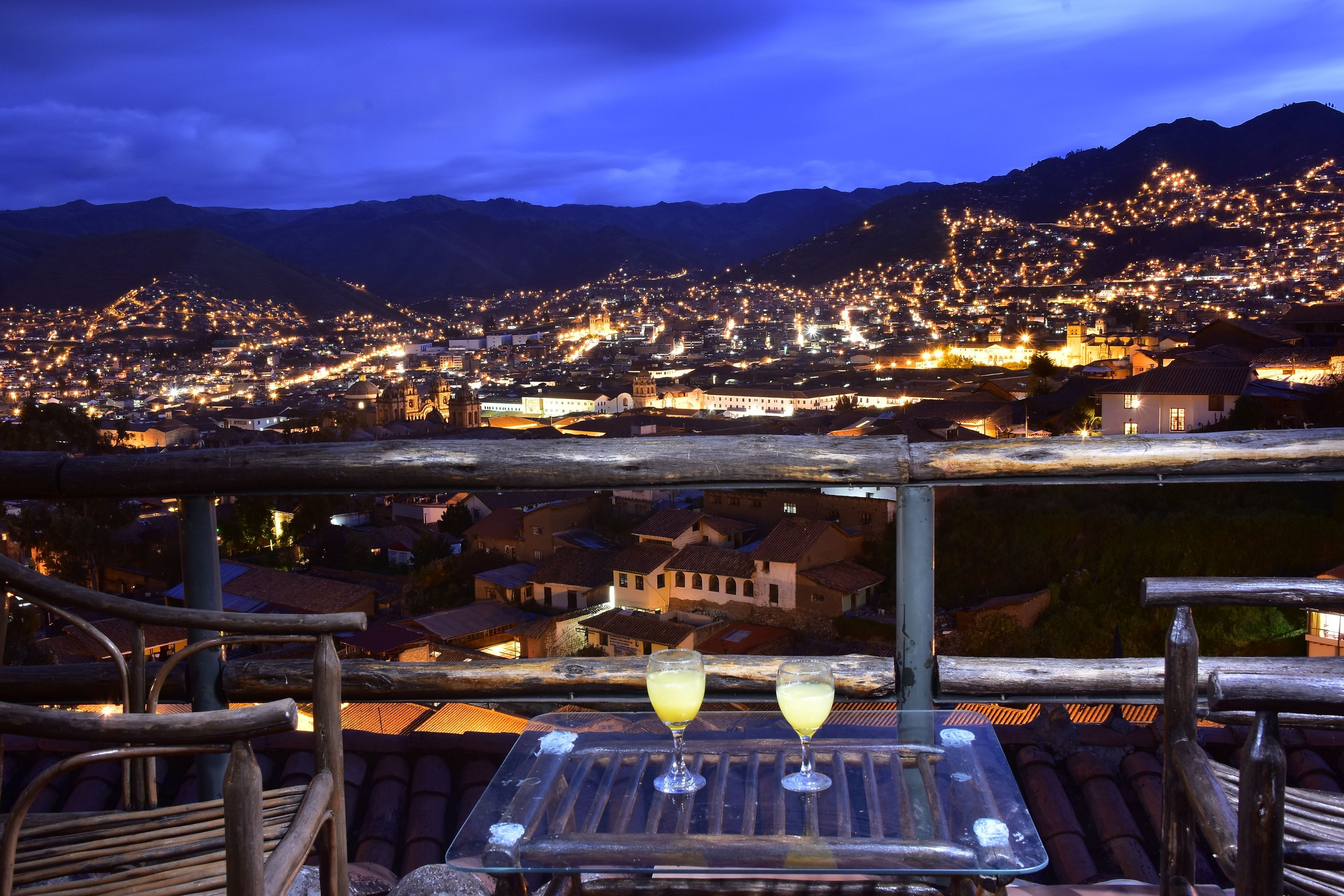 A terrace with a table and chairs overlooking a cityscape at night.