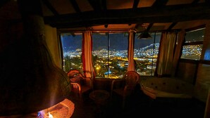 A cozy room with a large stone fireplace, a view of a cityscape at night, and a rustic wooden ceiling. - Casa de Campo Cusco (Cusco)