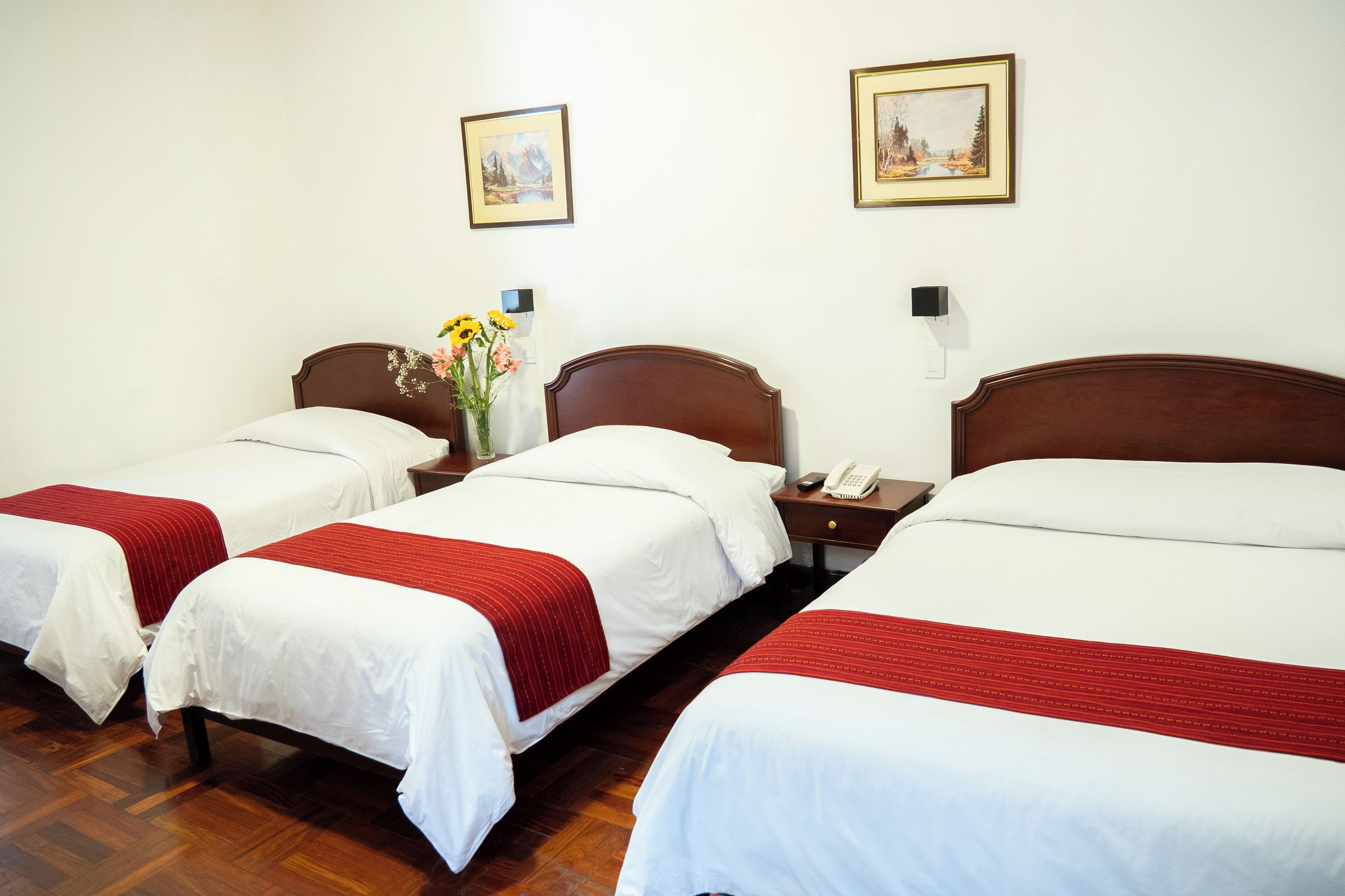 A hotel room with two single beds, a wooden headboard, a nightstand with a phone, and a wall-mounted light.