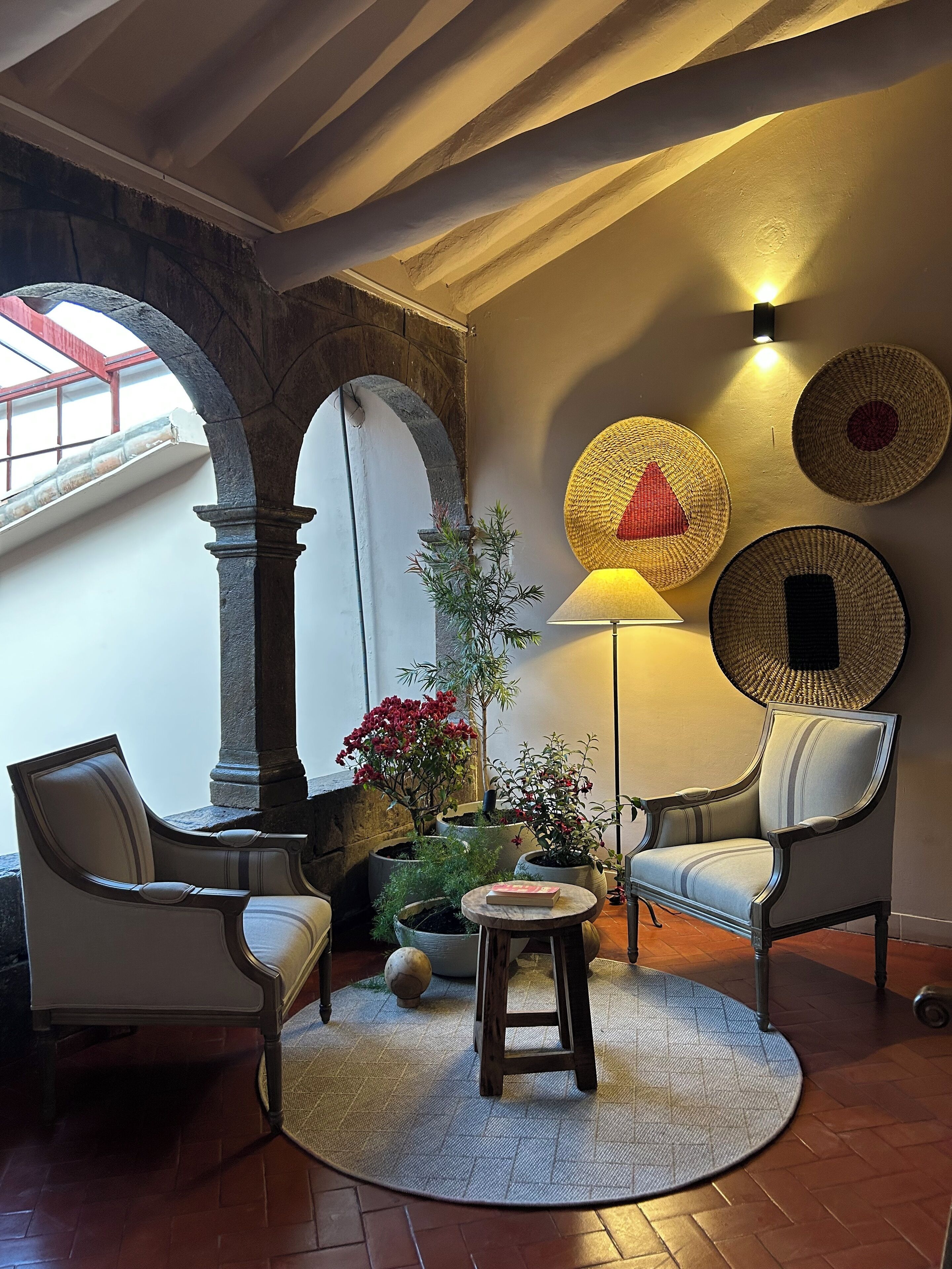 A cozy room with a stone archway, two chairs, a table, a lamp, and wall-mounted baskets.