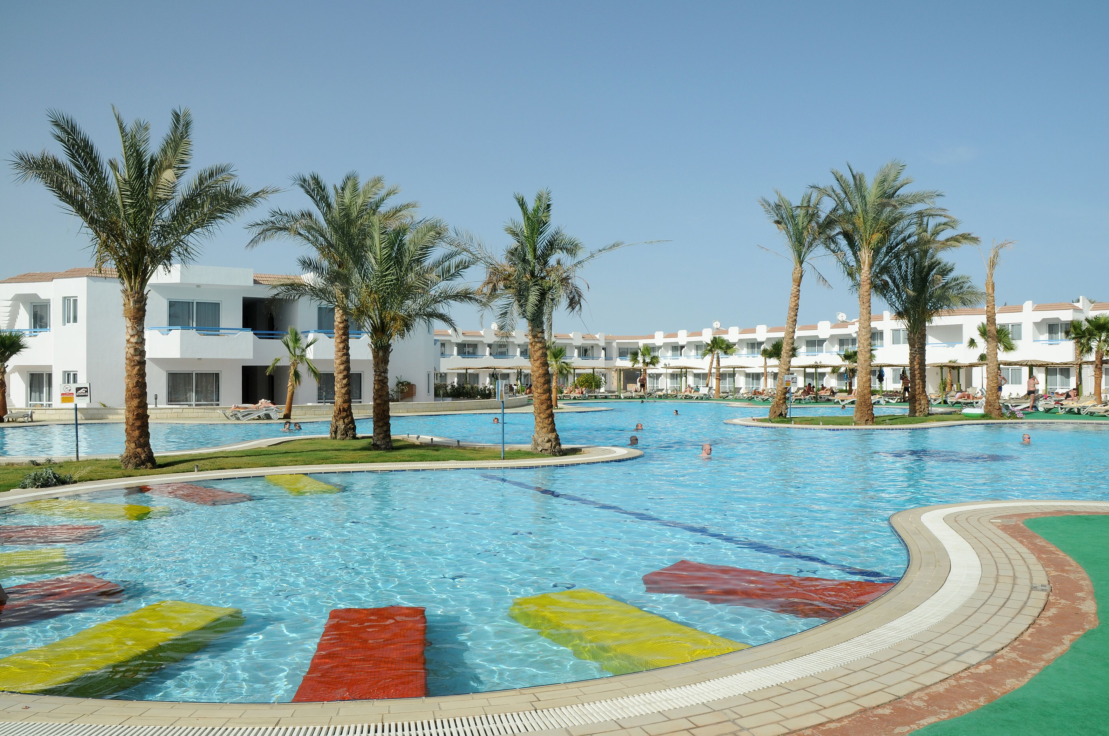 Une piscine bordée de palmiers et, au fond, un bâtiment d’hôtel.