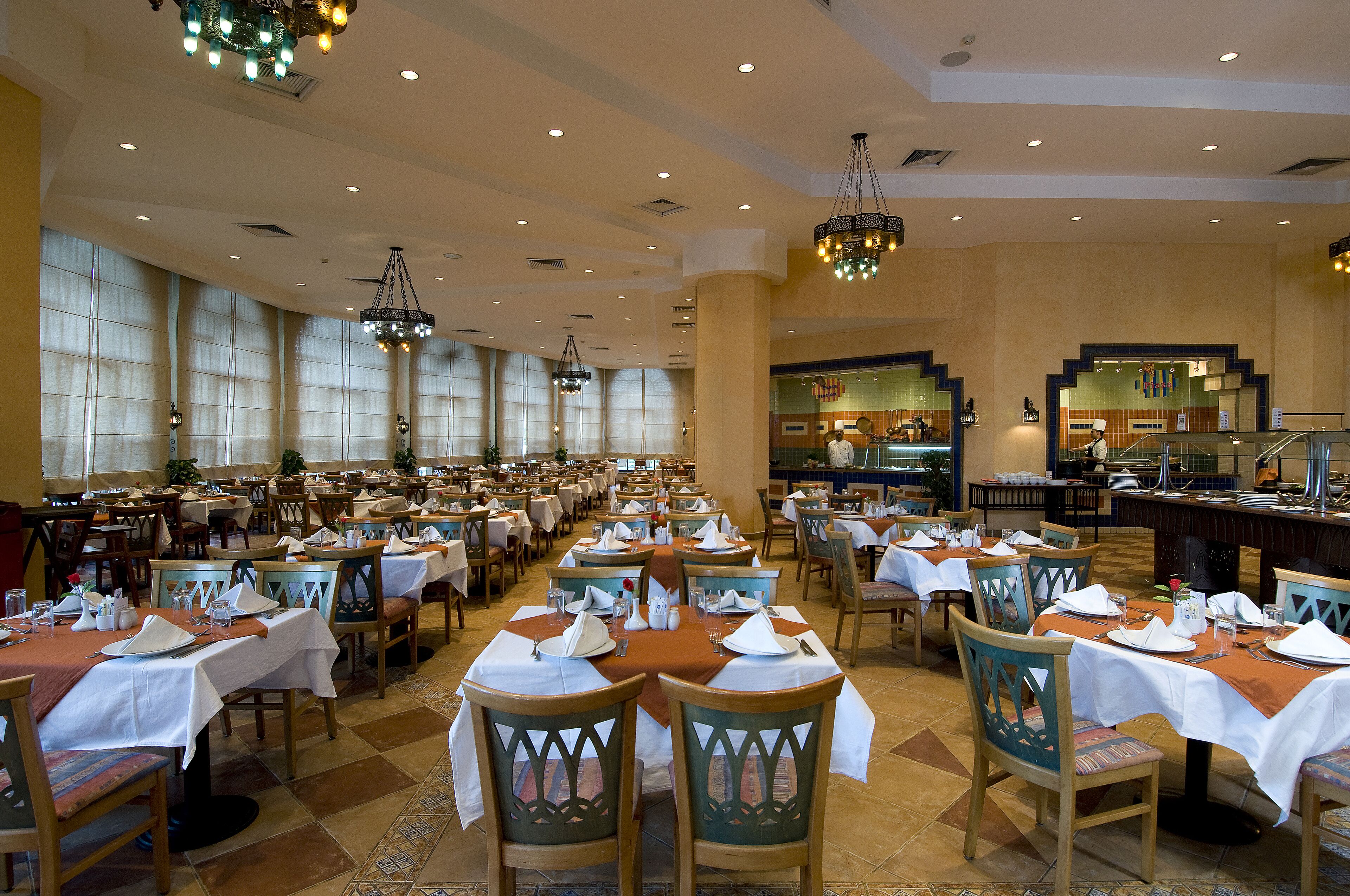 Un amplio comedor con varias mesas dispuestas para el servicio, grandes ventanales y una zona de bar central.