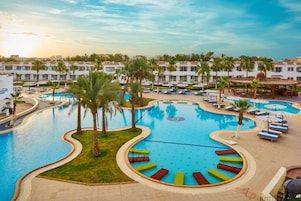 A resort pool area with multiple swimming pools, lounge chairs, and palm trees.