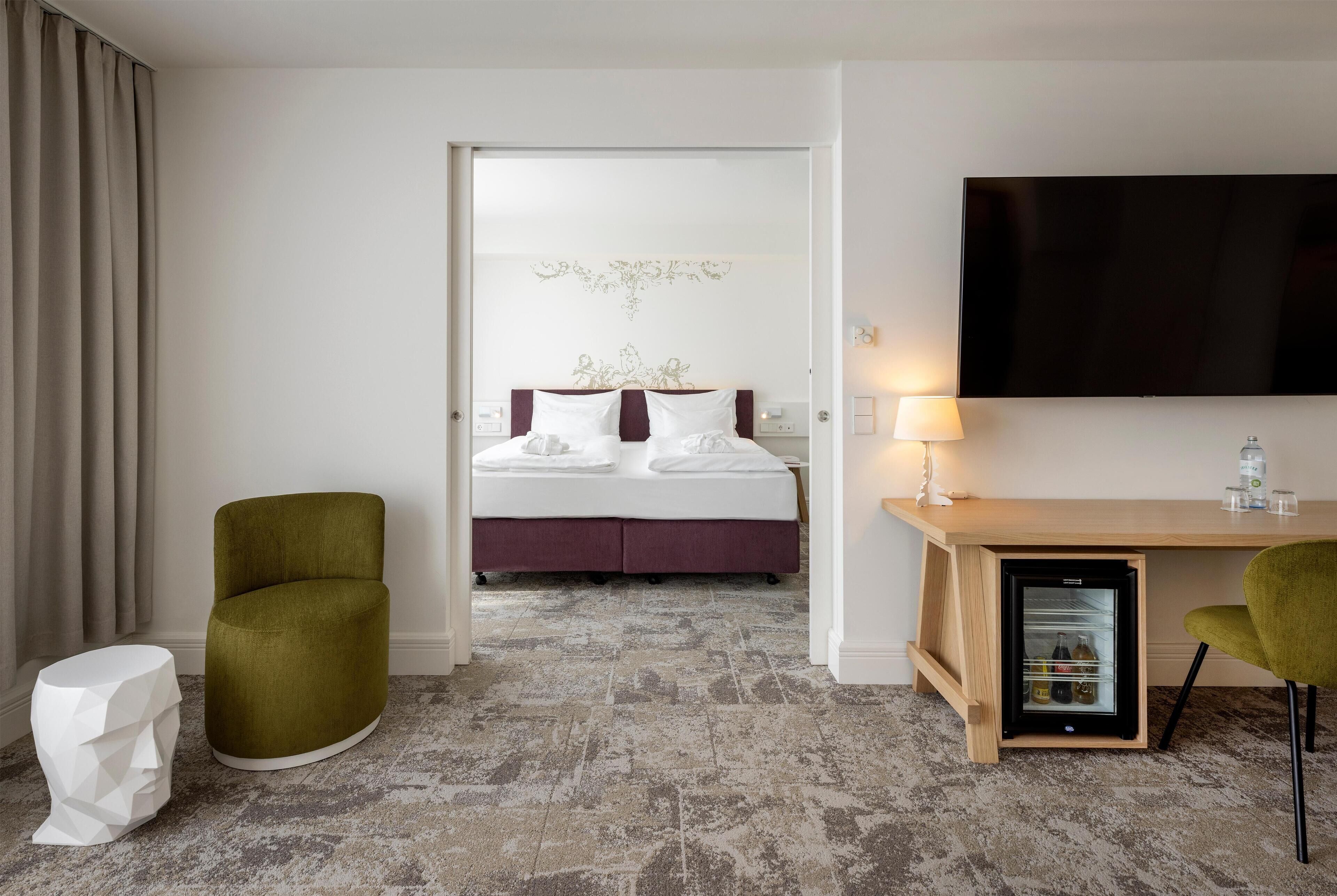 A hotel room with a bed, a desk, a television, a mini-fridge, and a chair.