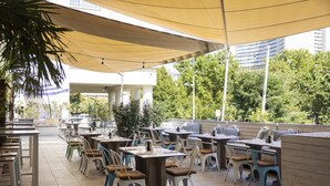 An outdoor patio area with tables and chairs, shaded by a large canopy, and surrounded by greenery. - ARCOTEL Kaiserwasser Vienna (Vienna)