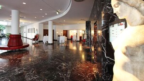 A lobby with marble flooring, a statue, and a red chair. - ARCOTEL Kaiserwasser Vienna (Vienna)