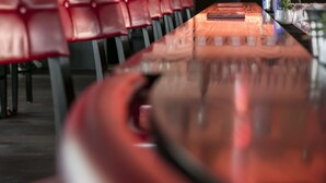 A bar with a long counter, red chairs, and shelves stocked with bottles. - ARCOTEL Kaiserwasser Vienna (Vienna)