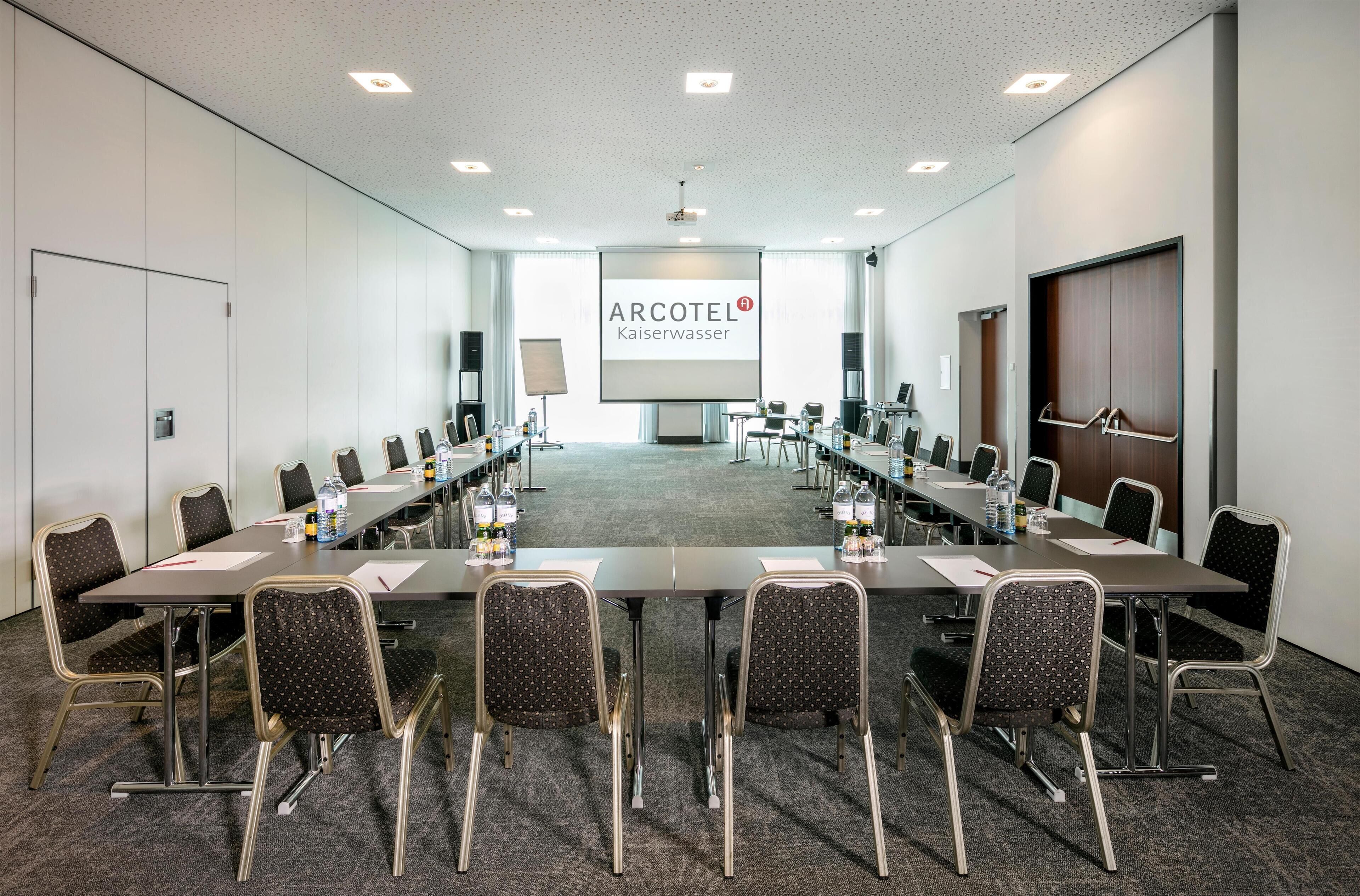 A conference room with a long table, chairs, a projector screen, and a presentation screen.