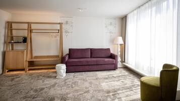 A modern room with a wooden bunk bed, a purple sofa, a green armchair, and a large window with sheer curtains.