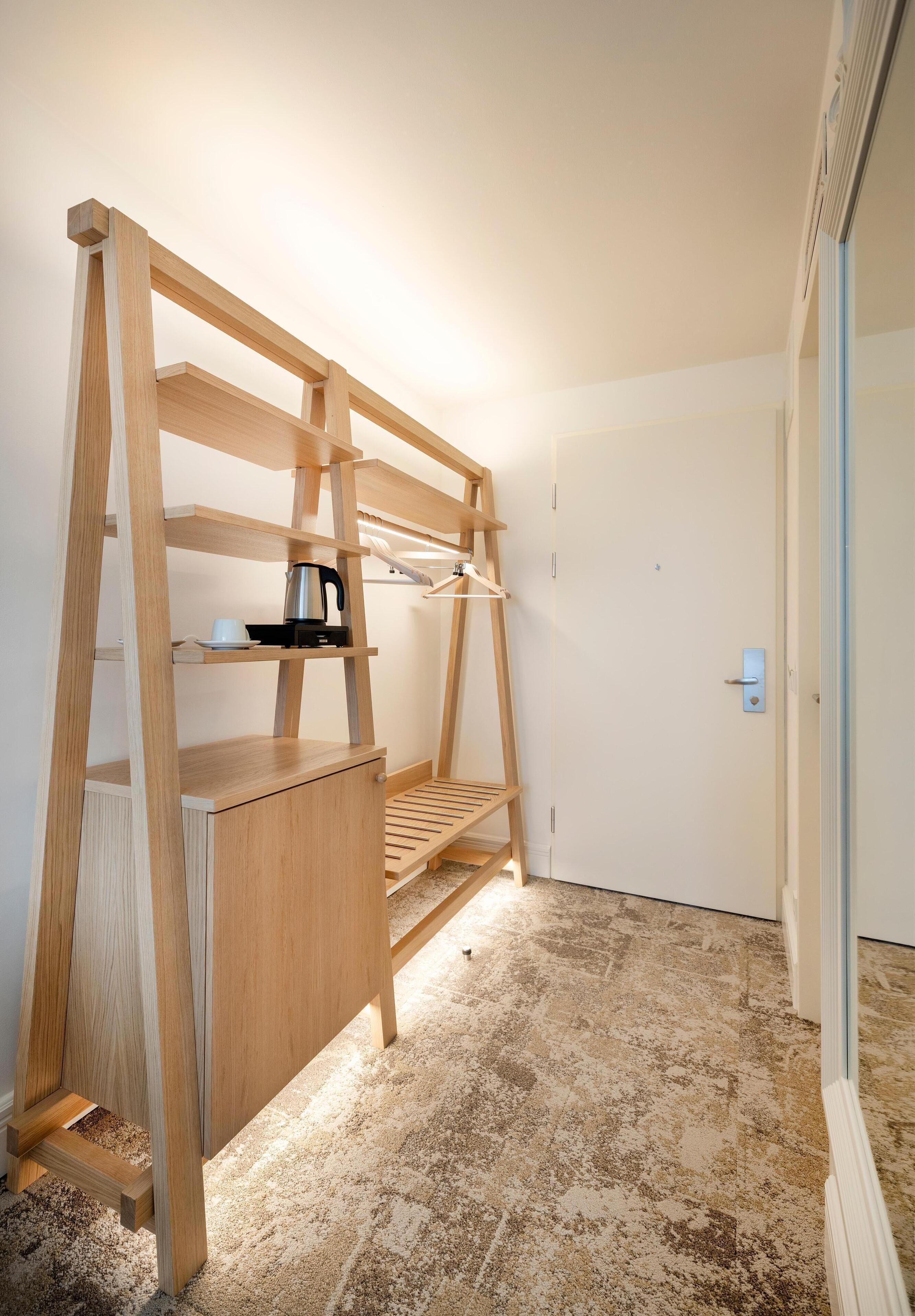 A compact, well-lit room with a wooden desk, shelves, and a radiator.