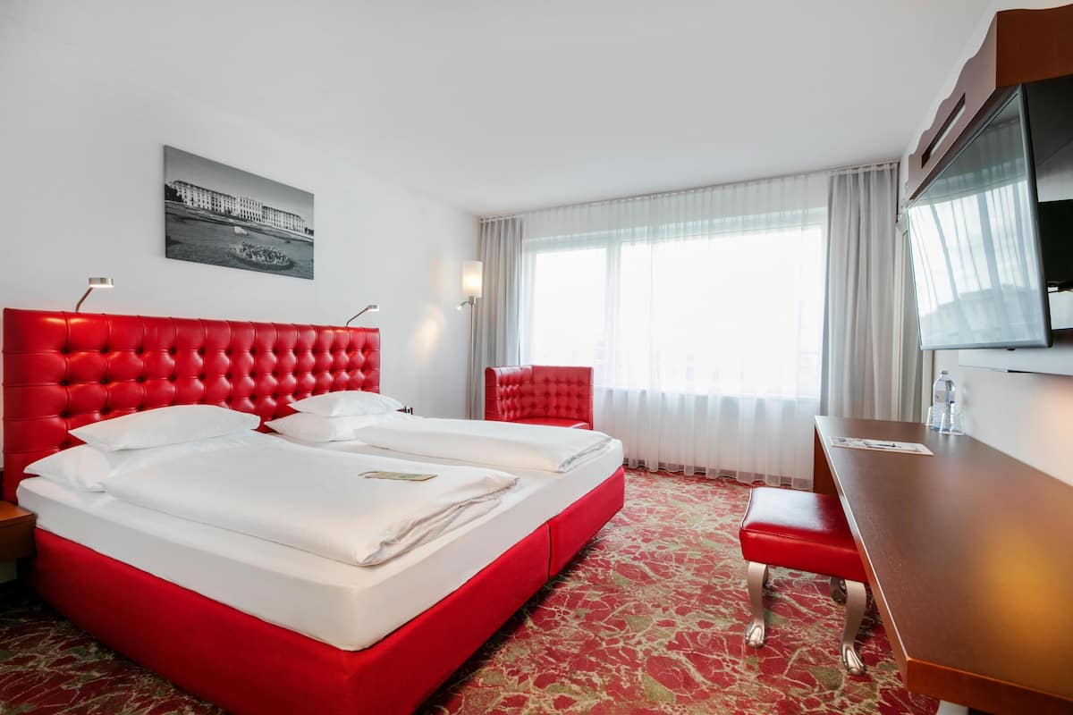 Habitación de hotel con cama roja, escritorio y televisión.
