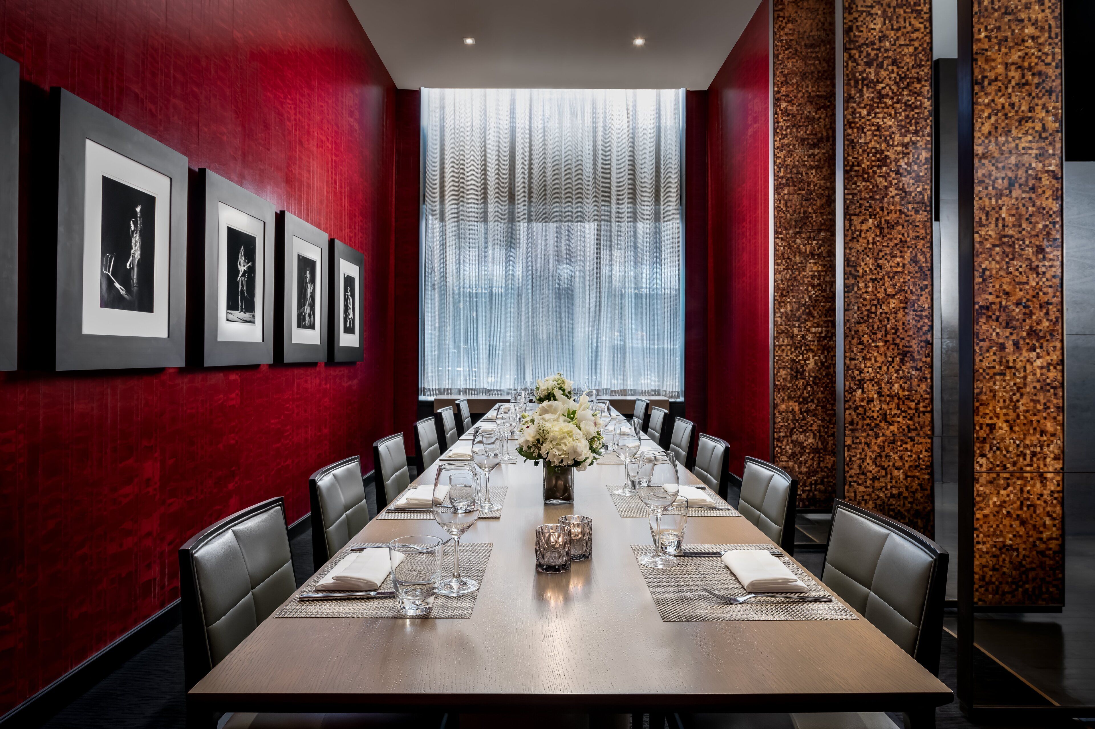 A conference room with a long table, chairs, framed pictures on the wall, and a large window with curtains.