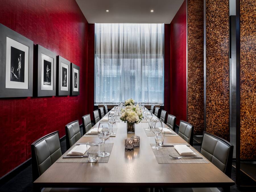 A conference room with a long table, chairs, framed pictures on the wall, and a large window with curtains.