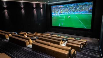 A cinema with rows of brown leather seats and a large screen displaying a soccer match.