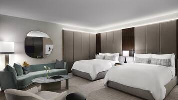 A modern hotel room with a large bed, a sofa, a round coffee table, and a mirror.