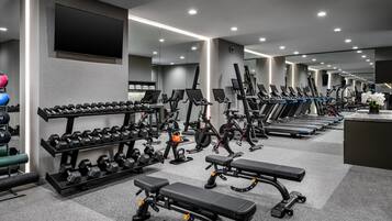 Une salle de sport moderne équipée de tapis de course, de vélos elliptiques et de poids libres.