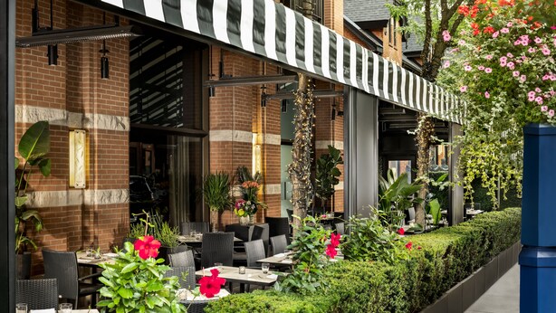 An outdoor cafe with brick walls, black and white striped awnings, and tables with chairs. - The Hazelton Hotel Toronto (Toronto)