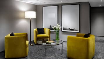 A modern lobby with yellow armchairs, a round glass table, and two large framed artworks on the wall.