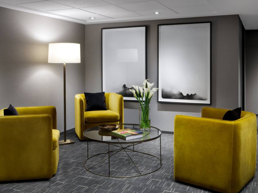 A modern lobby with yellow armchairs, a round glass table, and two large framed artworks on the wall.