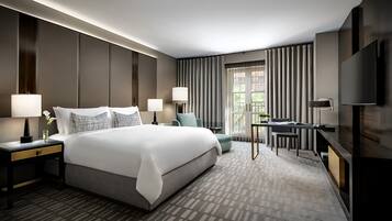Una habitación de hotel moderna con una cama grande, dos mesitas de noche con lámparas, un escritorio con una silla y un televisor en la pared.