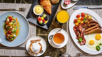 Ein reichhaltiges Frühstücksbuffet mit Croissants, Obst, Eiern, Speck, Toast und einer Tasse Tee.