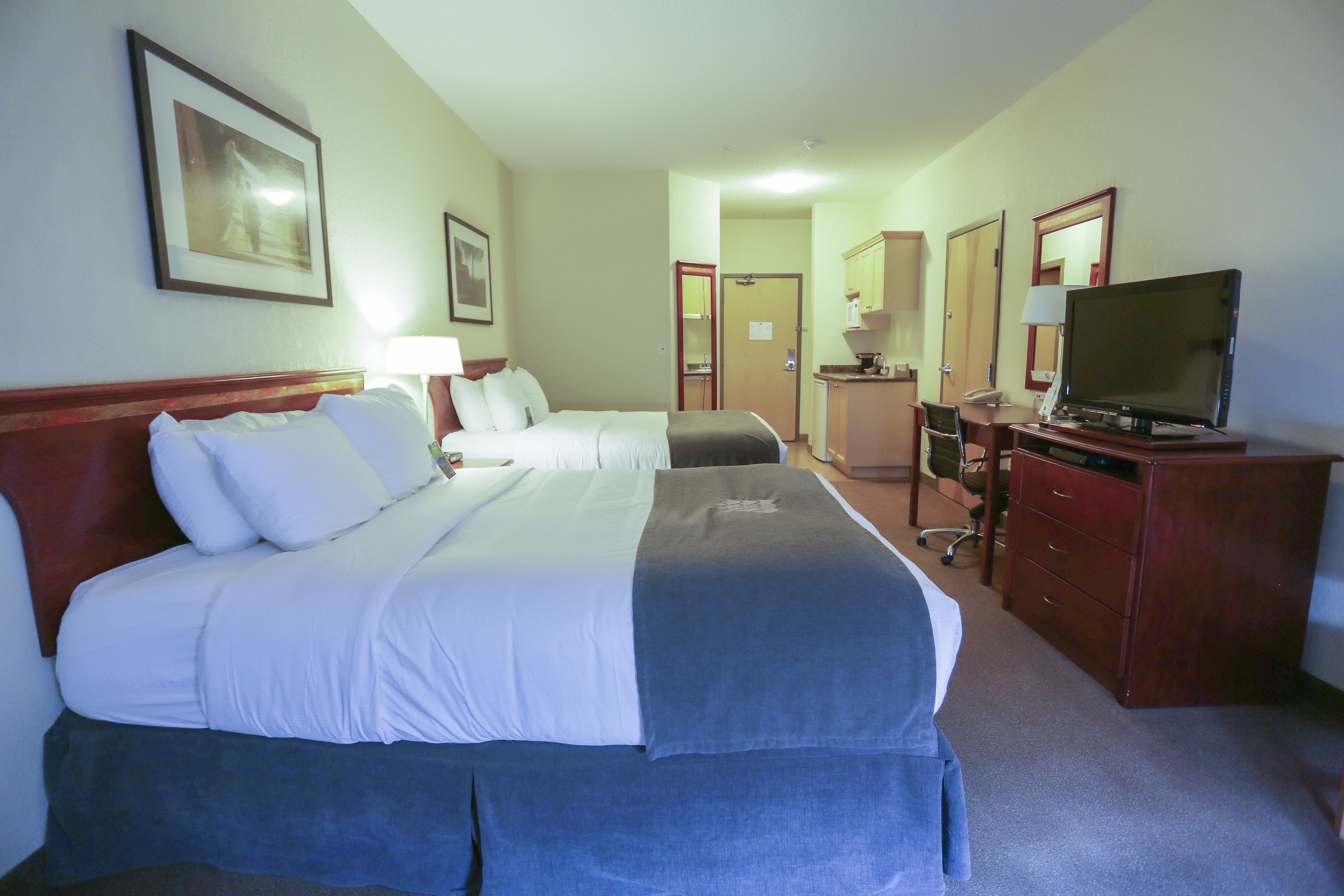 A hotel room with two beds, a desk with a television, and a mirror.