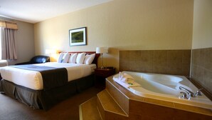 A hotel room with a bed, a bathroom with a bathtub, and a nightstand with a lamp.