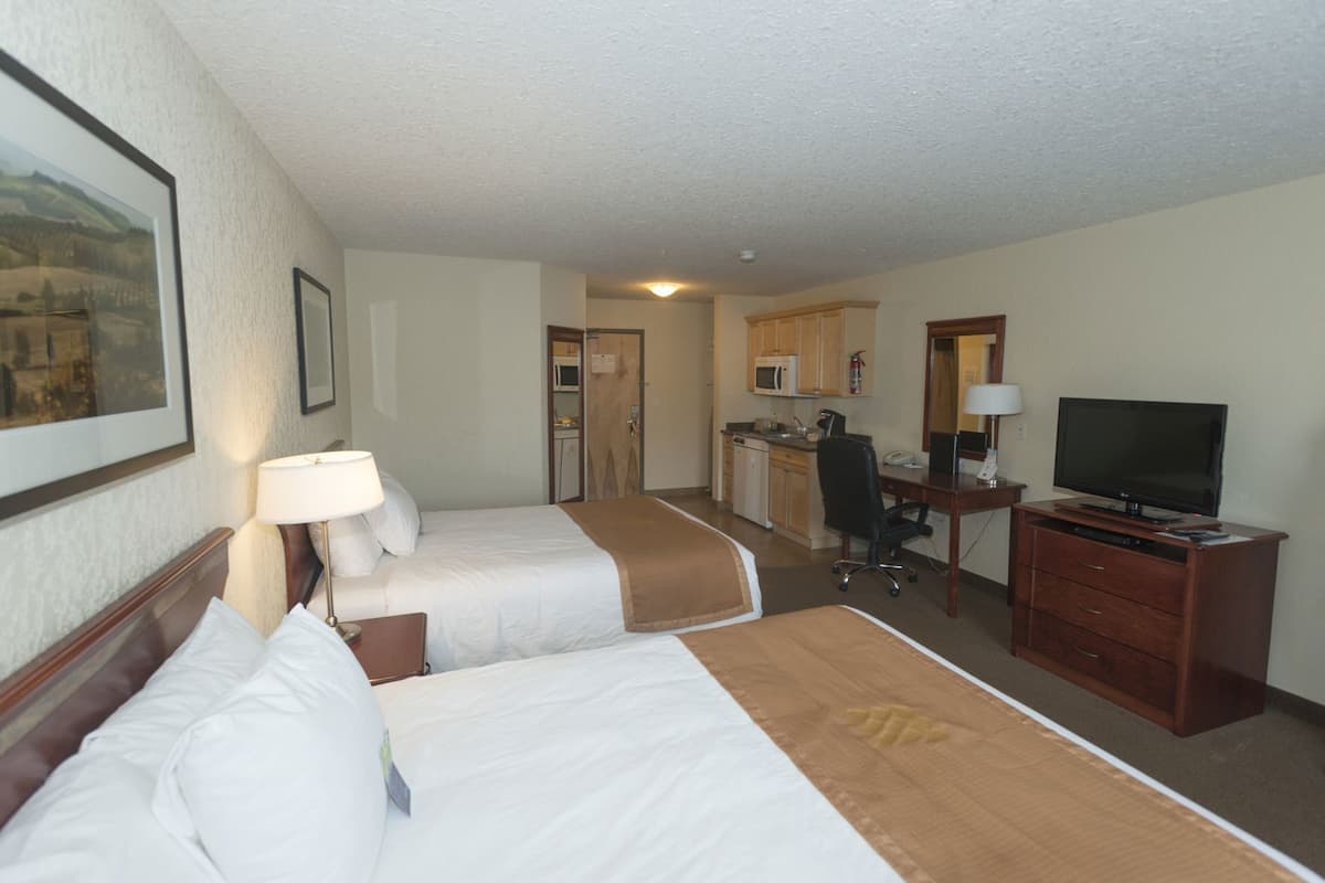 A hotel room with two beds, a desk, a television, and a kitchenette.