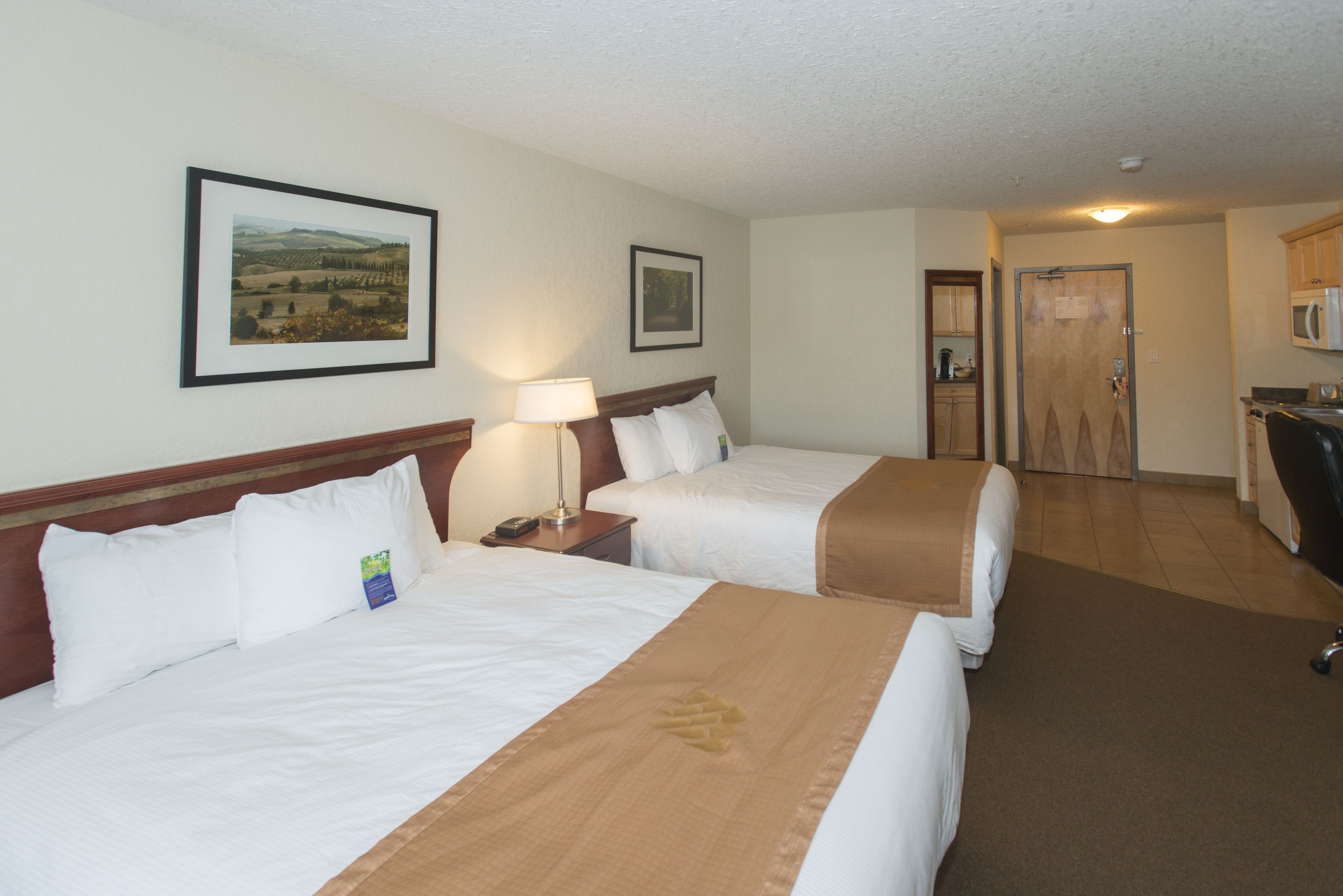 A hotel room with two beds, a desk, a microwave, and a door to the bathroom.