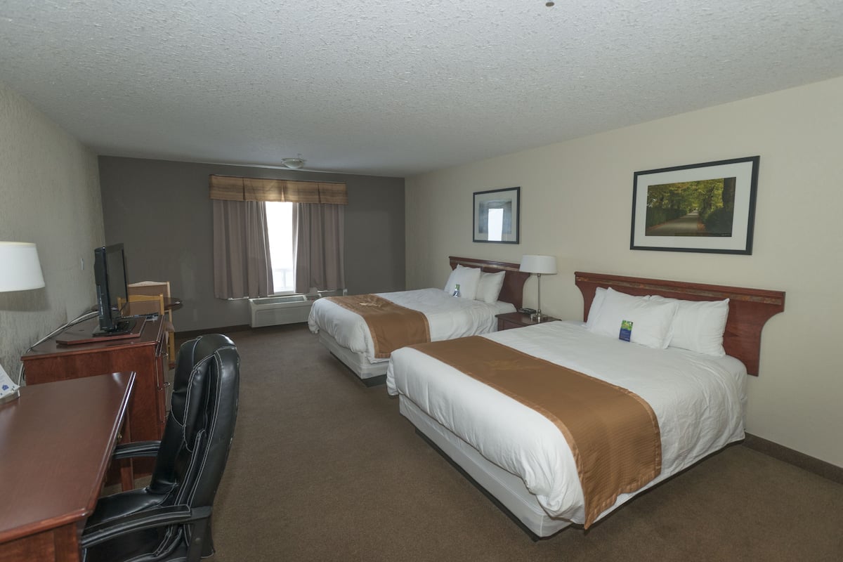 A hotel room with two beds, a desk, a chair, a TV, and a window with curtains.